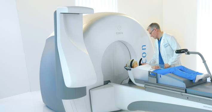 A man receiving Gamma Knife treatment in a medical room, with visible machinery and equipment.